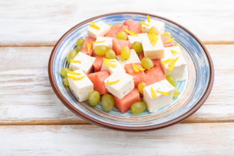 Vegetarian salad with watermelon, feta cheese, and grapes on blue ceramic plate on white wooden