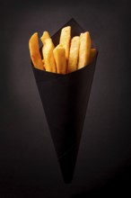 French fries, in black paper packaging, on a black background, close-up, selective focus