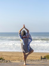 Woman performing yoga Tree pose Vrikshasanayoga, Atlantic Ocean Morocco, north Africa