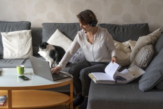 Woman, mid-50s, works from home, with laptop and communicates with colleagues via headset, home