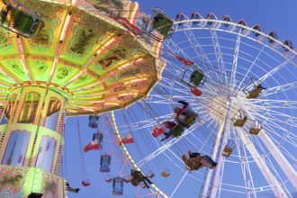 Illuminated chain carousel and Ferris wheel at night with cheerful people, funfair, wave flight,