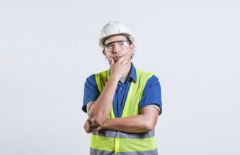 Young builder wondering looking up with hand on chin. Pensive builder man with hand on chin