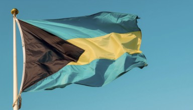 The flag of the Bahamas flutters in the wind, isolated against a blue sky