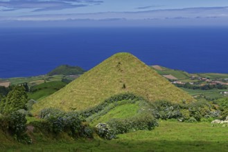 An isolated, green volcanic hill stands out, surrounded by agriculture and dense vegetation,