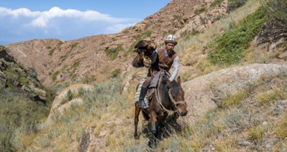 Traditional Kyrgyz eagle hunter with eagle in the mountains, hunting on horseback, near Kysyl-Suu,