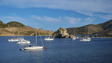 A harbour with several sailing boats and a large rock formation in the background, calm water and