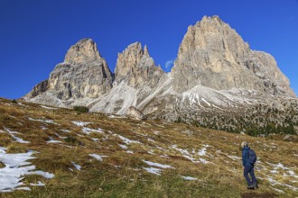 A man walks on a mountain meadow with snow-covered peaks at the Sella Pass of the Sella Group under