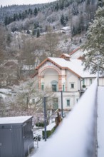 Snowy landscape with a traditional house and mountains in the background, spa garden, Bad Wildbad,