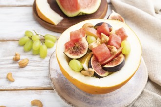 Vegetarian fruit salad of watermelon, grapes, figs, pear, orange, cashew on white wooden background