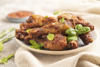 Smoked chicken legs with herbs and spices on a ceramic plate with linen textile on a brown concrete