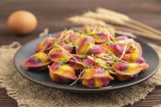 Rainbow colored dumplings with pepper, herbs, microgreen on brown wooden background and linen