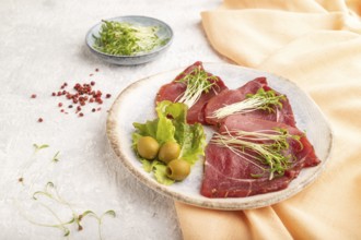 Slices of smoked salted meat with cilantro microgreen on gray concrete background and orange