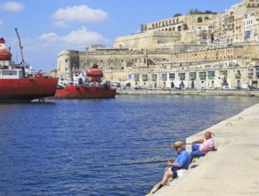 Men fishing historic waterfront buildings on quayside, Valletta, Malta, Europe