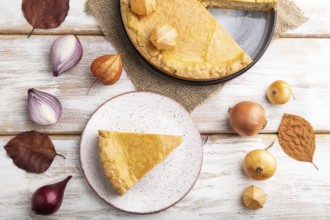 Autumn onion pie decorated with leaves and cup of coffee on white wooden background and linen