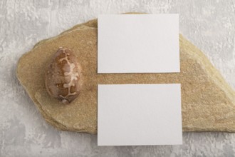 White paper business card, mockup with natural stone and seashell on gray concrete background.