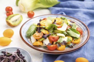 Vegetarian salad of pac choi cabbage, kiwi, tomatoes, kumquat, microgreen sprouts on a white