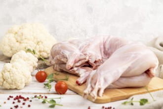 Whole raw rabbit with cauliflower, tomatoes and spices on a white wooden background and linen