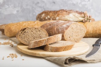 Sliced bread with different kinds of fresh baked bread on a white wooden background. side view,