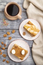 Honey cake with milk cream, caramel, almonds and a cup of coffee on a gray wooden background and