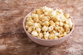 Popcorn with caramel in ceramic bowl on brown concrete background. Side view, close up