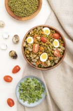 Mung bean porridge with quail eggs, tomatoes and microgreen sprouts on a white wooden background