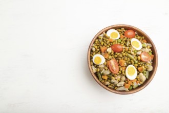 Mung bean porridge with quail eggs, tomatoes and microgreen sprouts on a white wooden background.