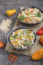 Pearl barley porridge with vegetables in blue ceramic bowls on a black concrete background and