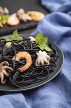 Black cuttlefish ink pasta with shrimps or prawns and small octopuses on black concrete background