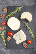 Blue cheese and various types of cheese with rosemary and tomatoes on black slate board on a black