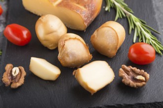 Smoked cheese and various types of cheese with rosemary and tomatoes on black slate board on a