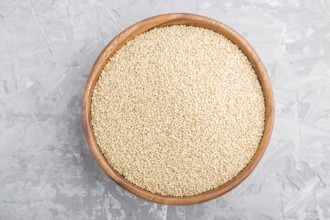 Wooden bowl with raw white quinoa seeds on a gray concrete background. Top view, flat lay, close up