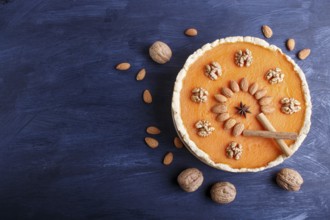 Traditional american sweet pumpkin pie decorated with nuts, on dark blue wooden background. top