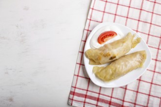 Cabbage rolls with beef, rice and vegetables on a linen tablecloth on a white wooden background.