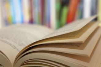 Close-up of an open book, behind it a blurred bookshelf