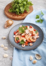 Boiled shrimps or prawns and small octopuses with herbs on a blue ceramic plate on a gray concrete