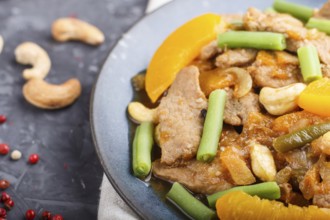 Fried pork with peaches, cashew and green beans on a black concrete background. Top view, close up,