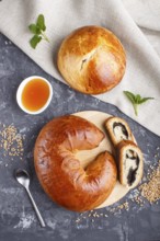 Homemade yeast buns and rolls with poppy seeds and honey on a black concrete background. top view,