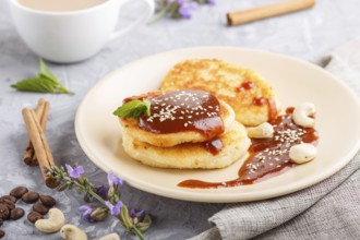 Cheese pancakes with caramel sauce on a beige ceramic plate and a cup of coffee on a gray concrete