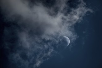 The crescent of the waxing moon in the second quarter shines in a cloudy, dark blue sky,