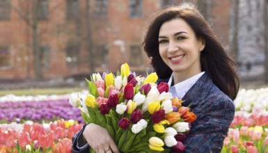 A smiling woman with a bouquet of fresh tulips stands in a park, AI generated, AI generated