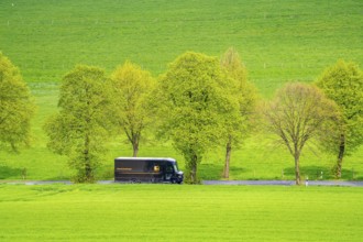 UPS delivery van on a country road, green fields, meadows, trees line the 2-lane road, spring, near