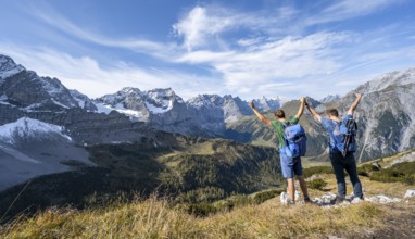 Two mountaineers hand in hand with outstretched arms, on a hiking trail, mountain panorama with