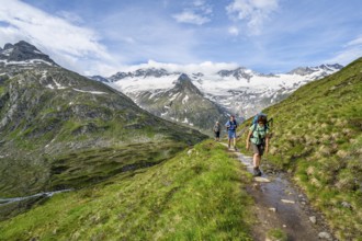 Three mountaineers on a hiking trail in a picturesque mountain landscape, mountain peak with snow