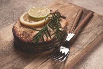 Salmon steak, fried, on a cutting board, top view, rosemary, lemon and lime, homemade, one serving,