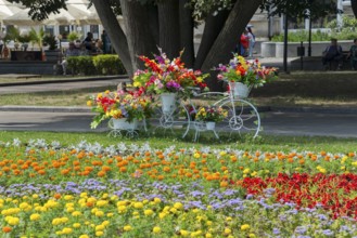 A white bicycle decorated with colourful flowers stands in a blooming park, Bicycle decorated with