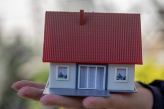 Symbolic image Desire to own a home: woman holding a model house in her hand