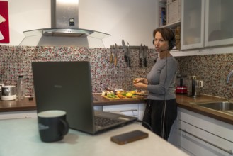 Woman, mid-50s, works from home, with laptop and communicates with colleagues via headset, home