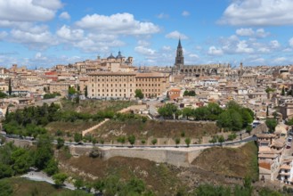 Panorama of Toledo with historic buildings, a cathedral and trees under a blue sky with clouds,