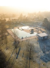 The morning sun casts long shadows over a swimming pool with frost-covered grass and trees, ENCW