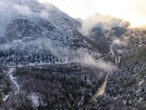 Aerial view of a winding road through a wintry forest in the mountains at twilight, Alpenstraße,